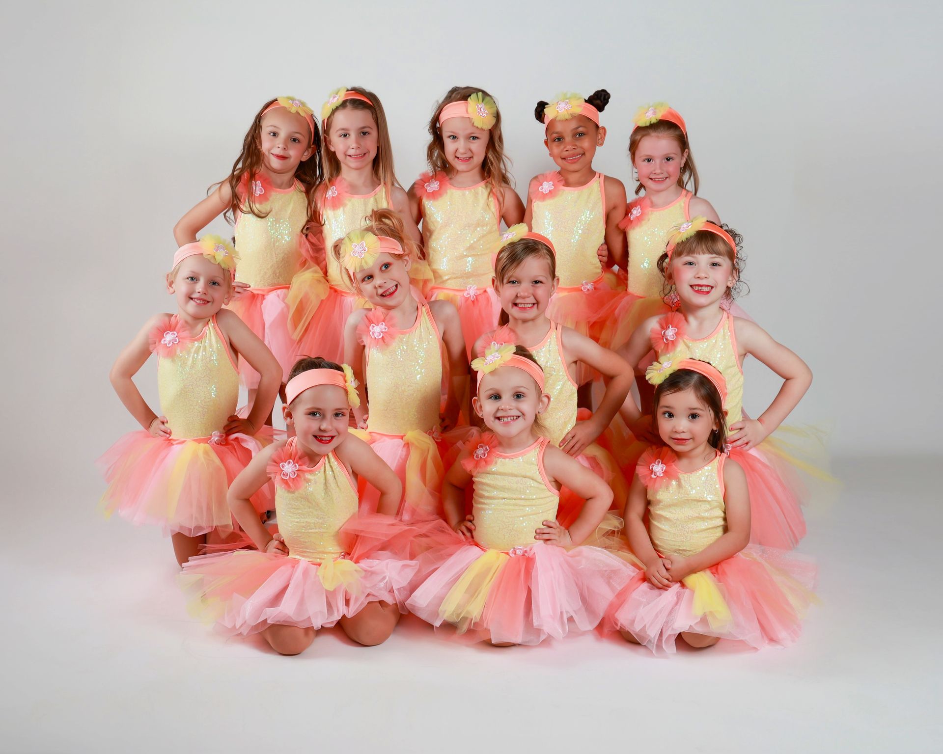 Group of young girls in matching yellow and pink dance costumes posing for a photo.