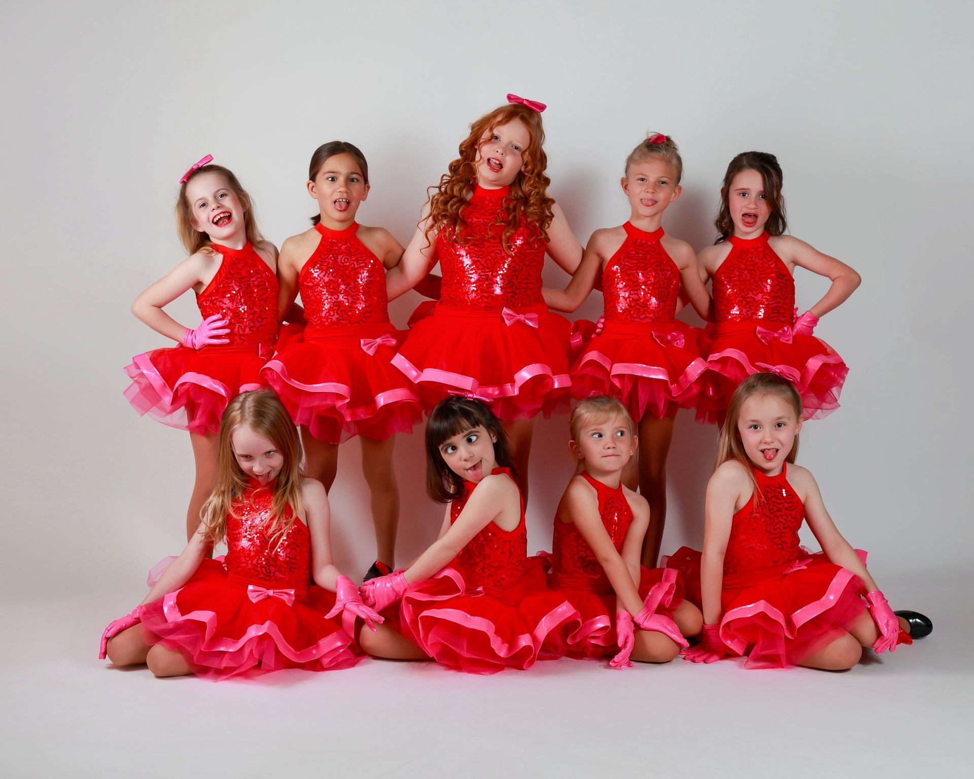 A group of young girls in red sparkly dresses and pink gloves striking poses.