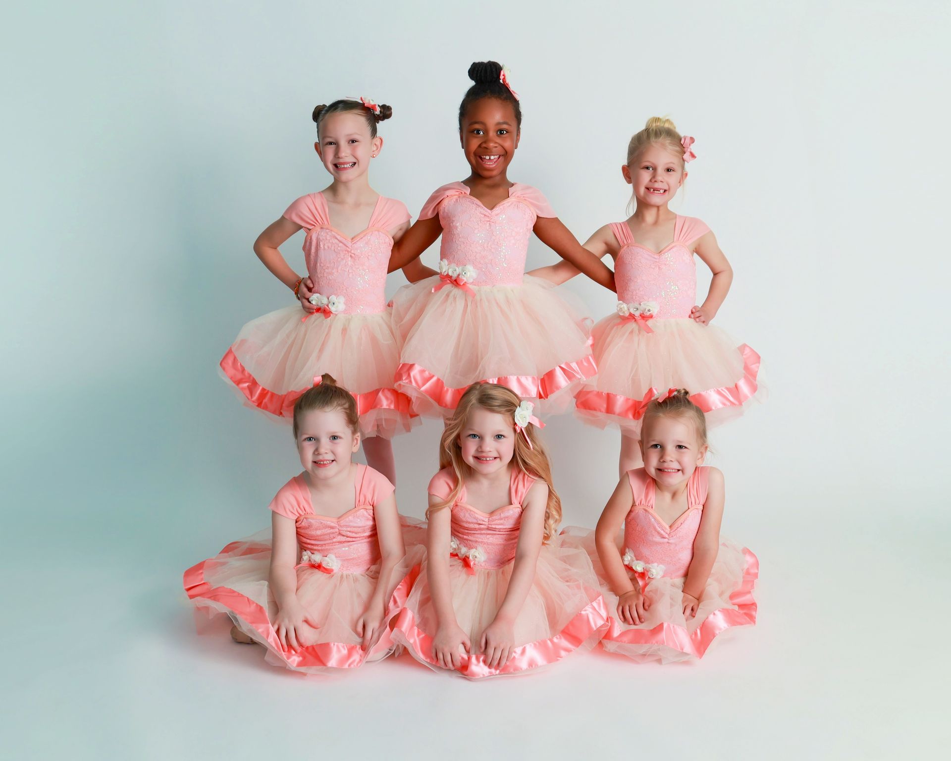 Seven young girls in pink tutus pose against a white backdrop.