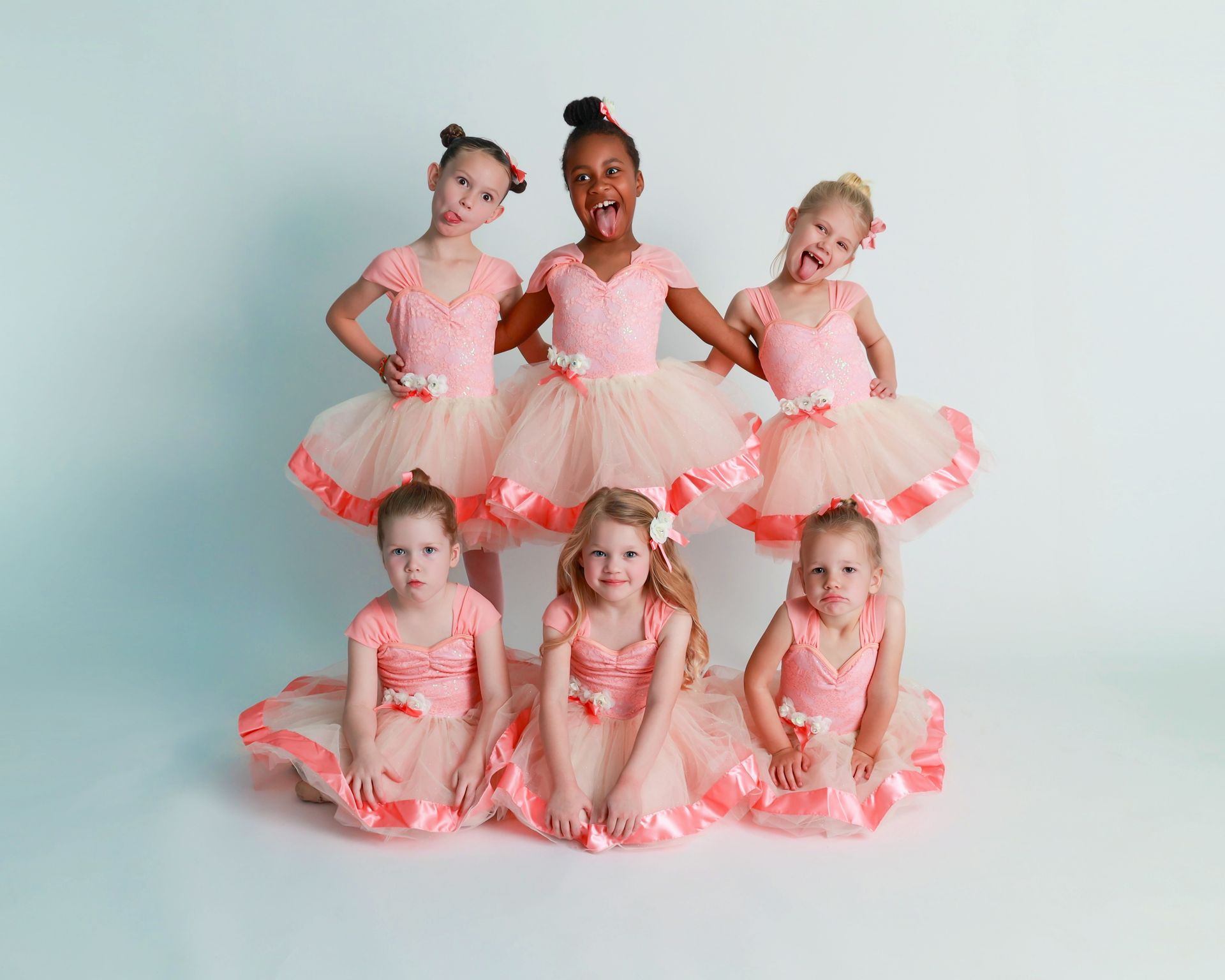 Seven young ballerinas in pink tutus posing playfully against a white background.