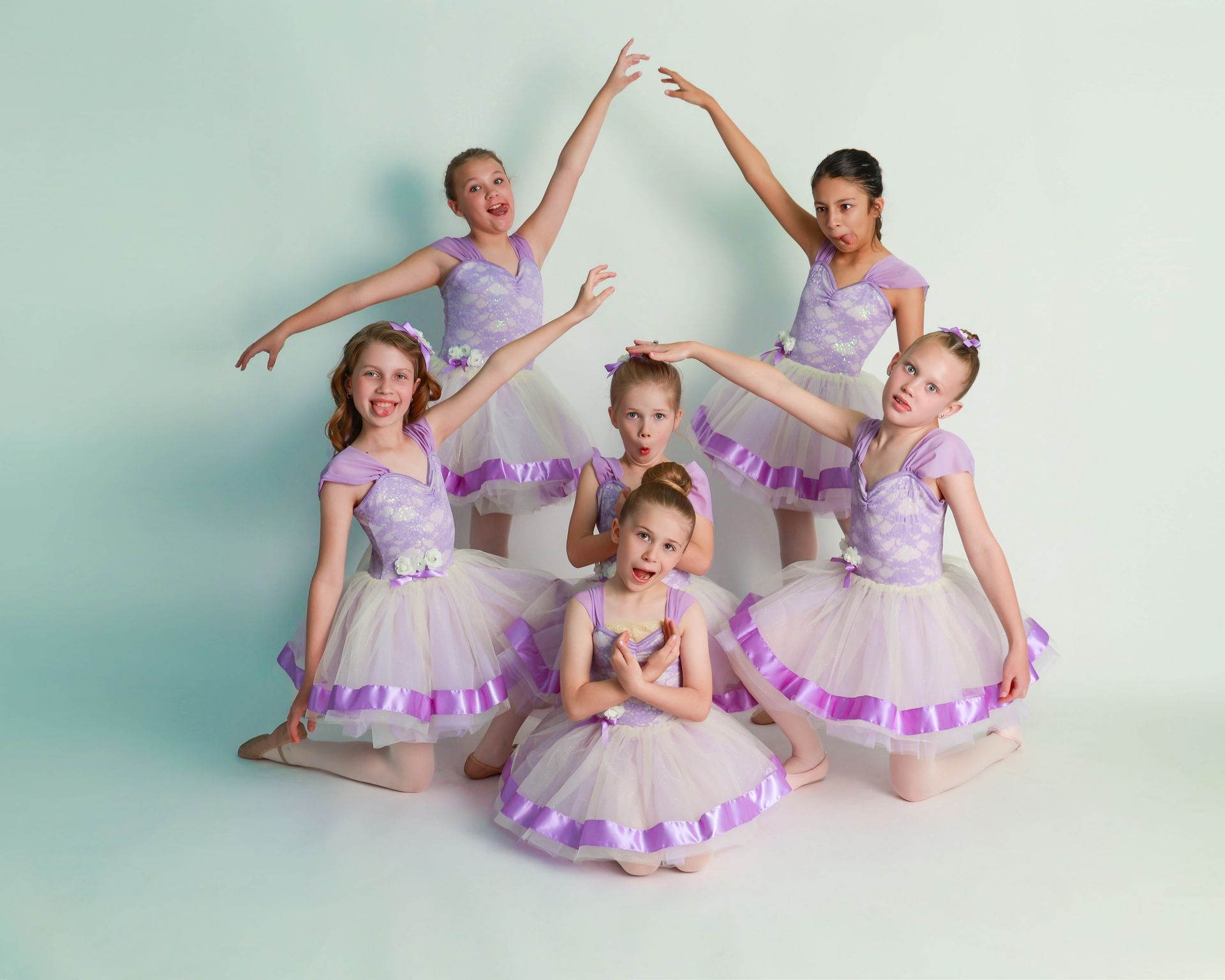 Group of young girls in lavender ballet costumes posing in a studio.