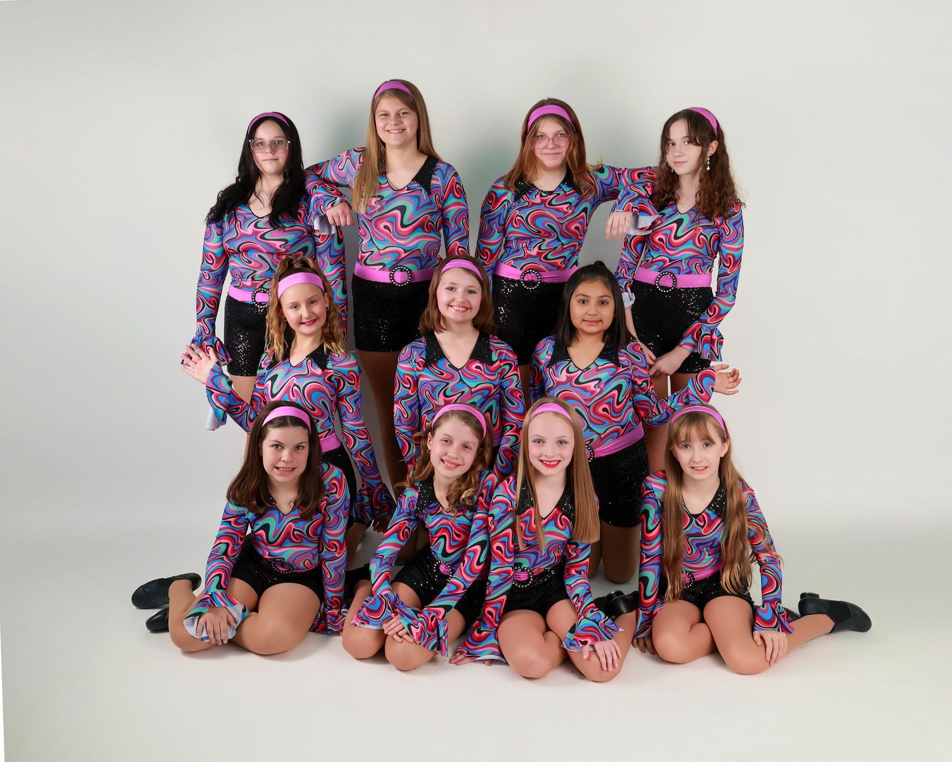 A group of young female dancers in colorful outfits, posing together in a studio setting.