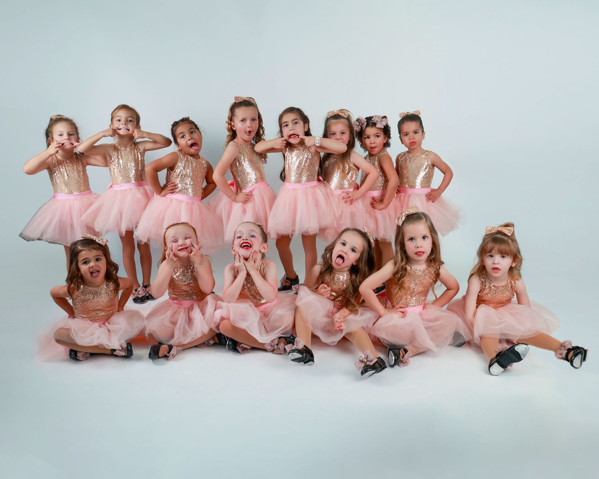 Group of young girls in pink tutus making funny faces, posing against a white background.