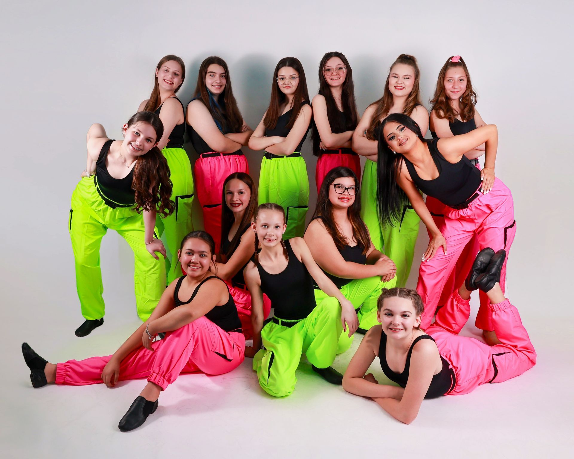 Teenage dancers in neon pink and green pants and black tops pose in a studio.