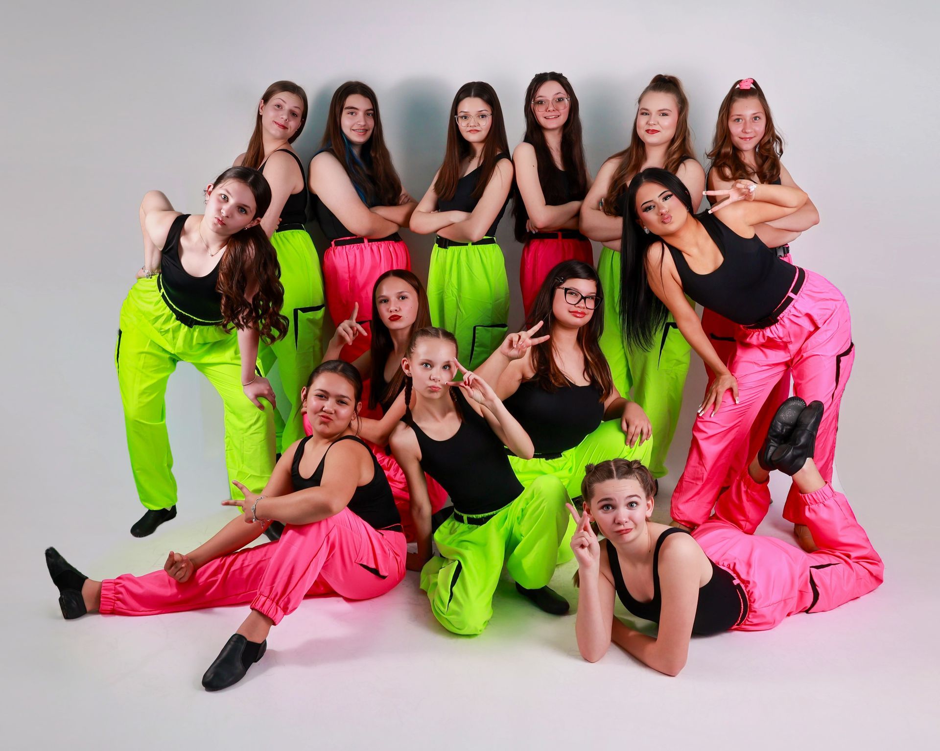 Dance group poses; neon pink/green outfits, black tops, gray backdrop.