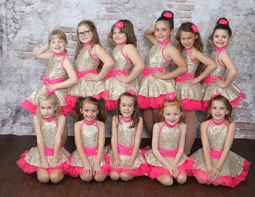 Ten young girls in gold and pink dance dresses pose for a group photo.