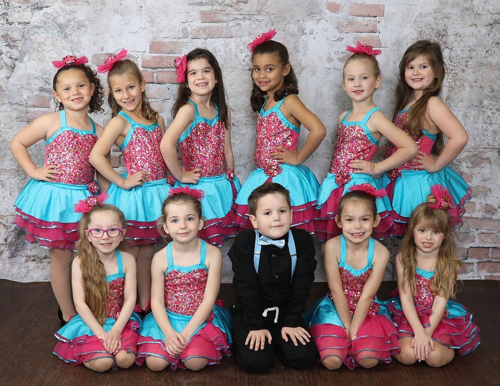 Group of children in matching dance costumes, posing in front of a brick wall.