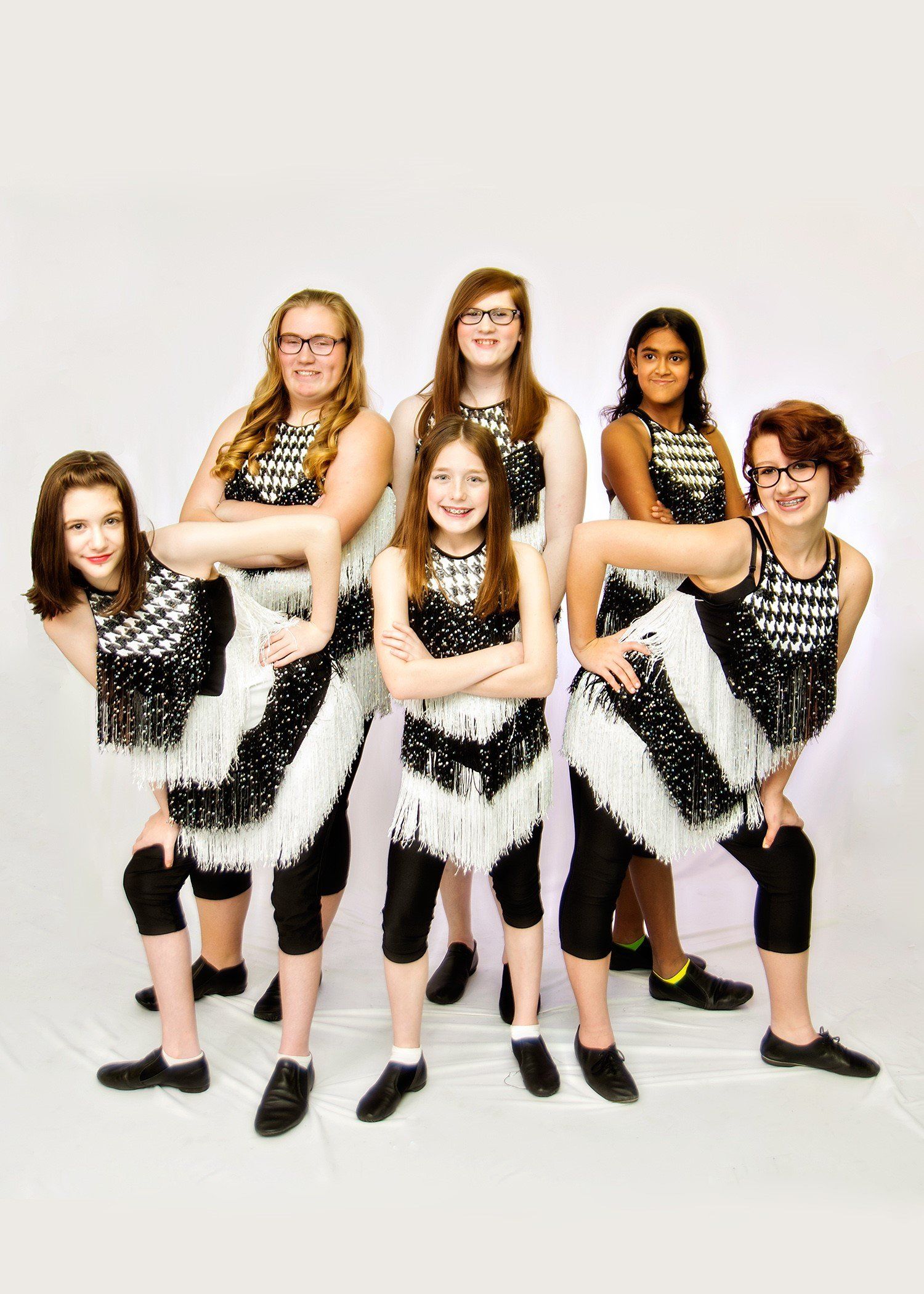 Six young dancers in black and white costumes pose, bending knees.