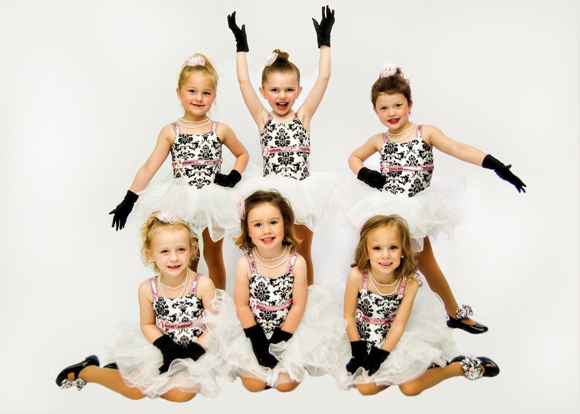 Young girls in matching white tutus, black gloves, and patterned tops pose for a group photo.