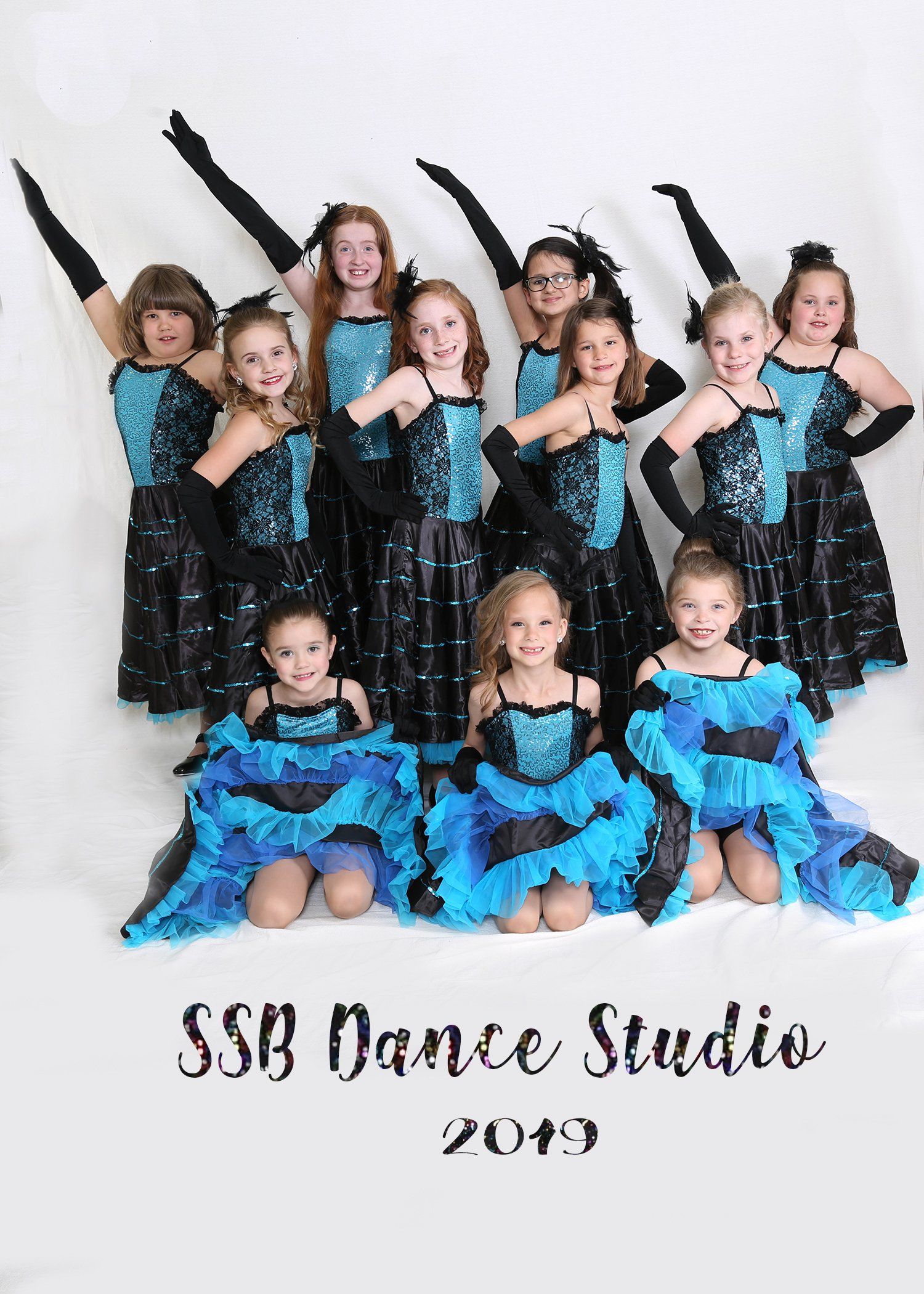 Group of young dancers in sparkly turquoise and black costumes, posing with arms raised. 