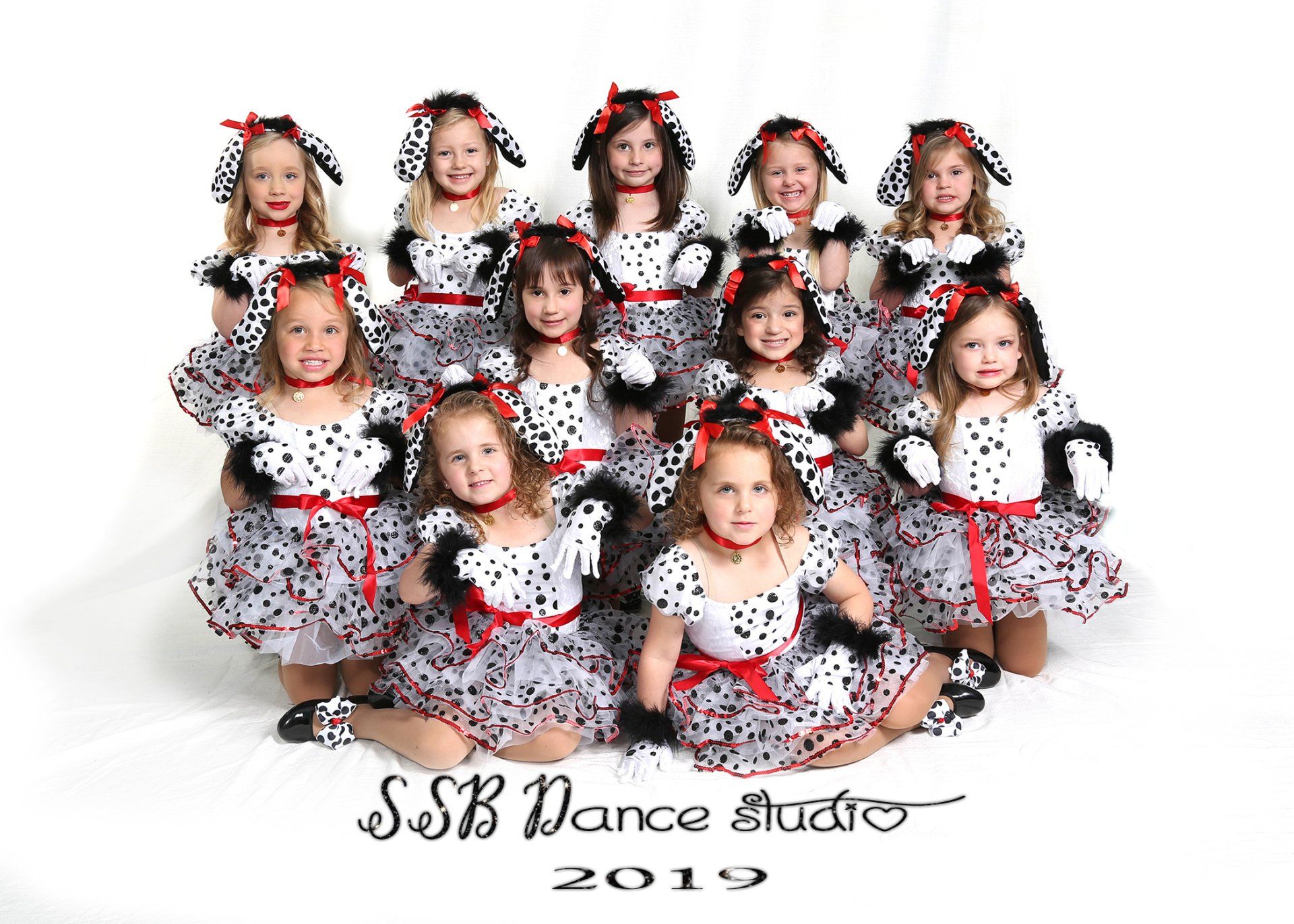 Group of young girls in Dalmatian costumes posing for a studio portrait, wearing black and white dresses with red accents.