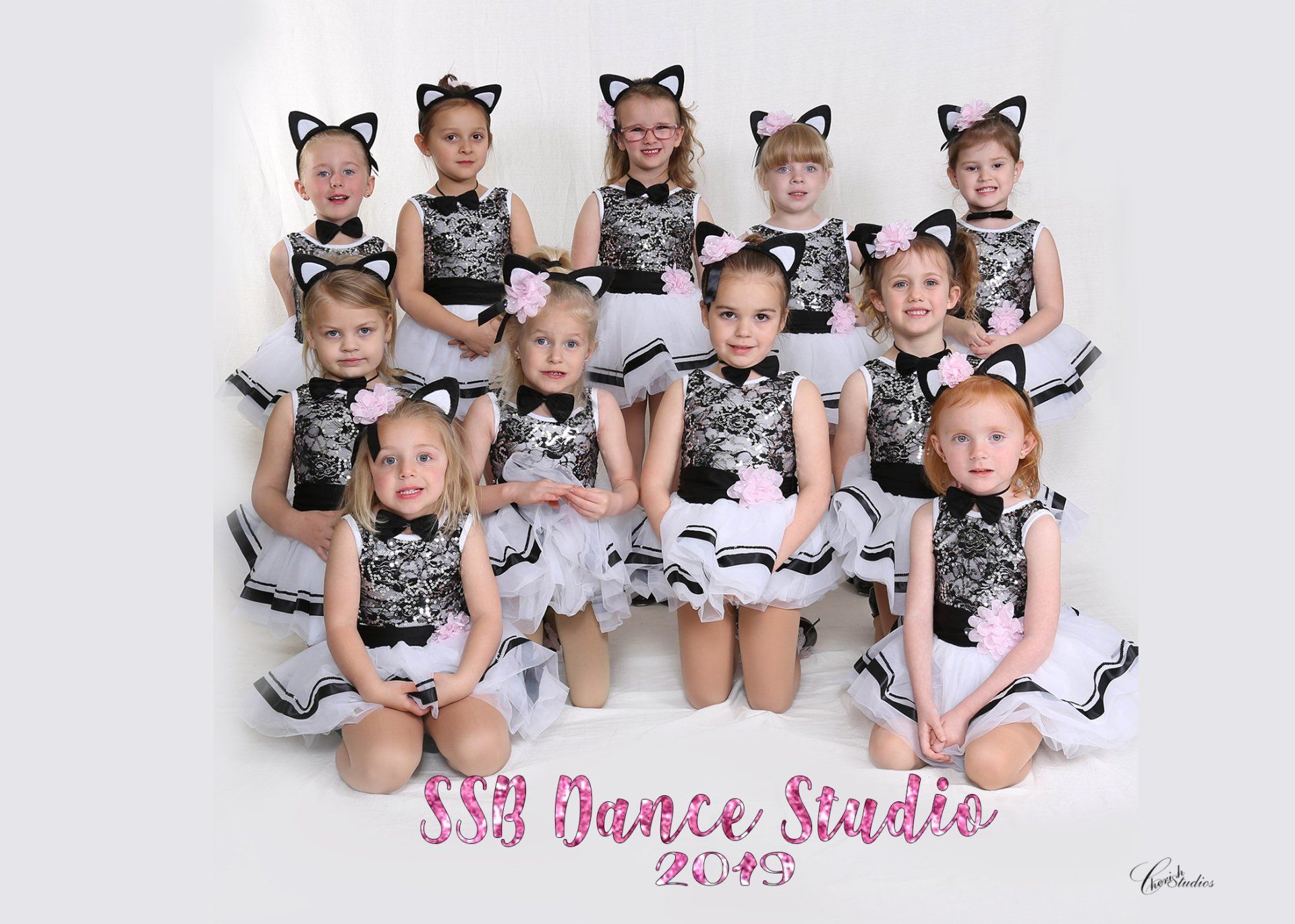 Group of young dancers in cat costumes, smiling. Black and white outfits, studio setting.