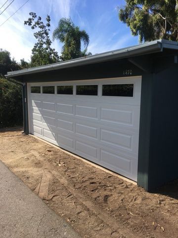A white garage door is sitting next to a dirt road.