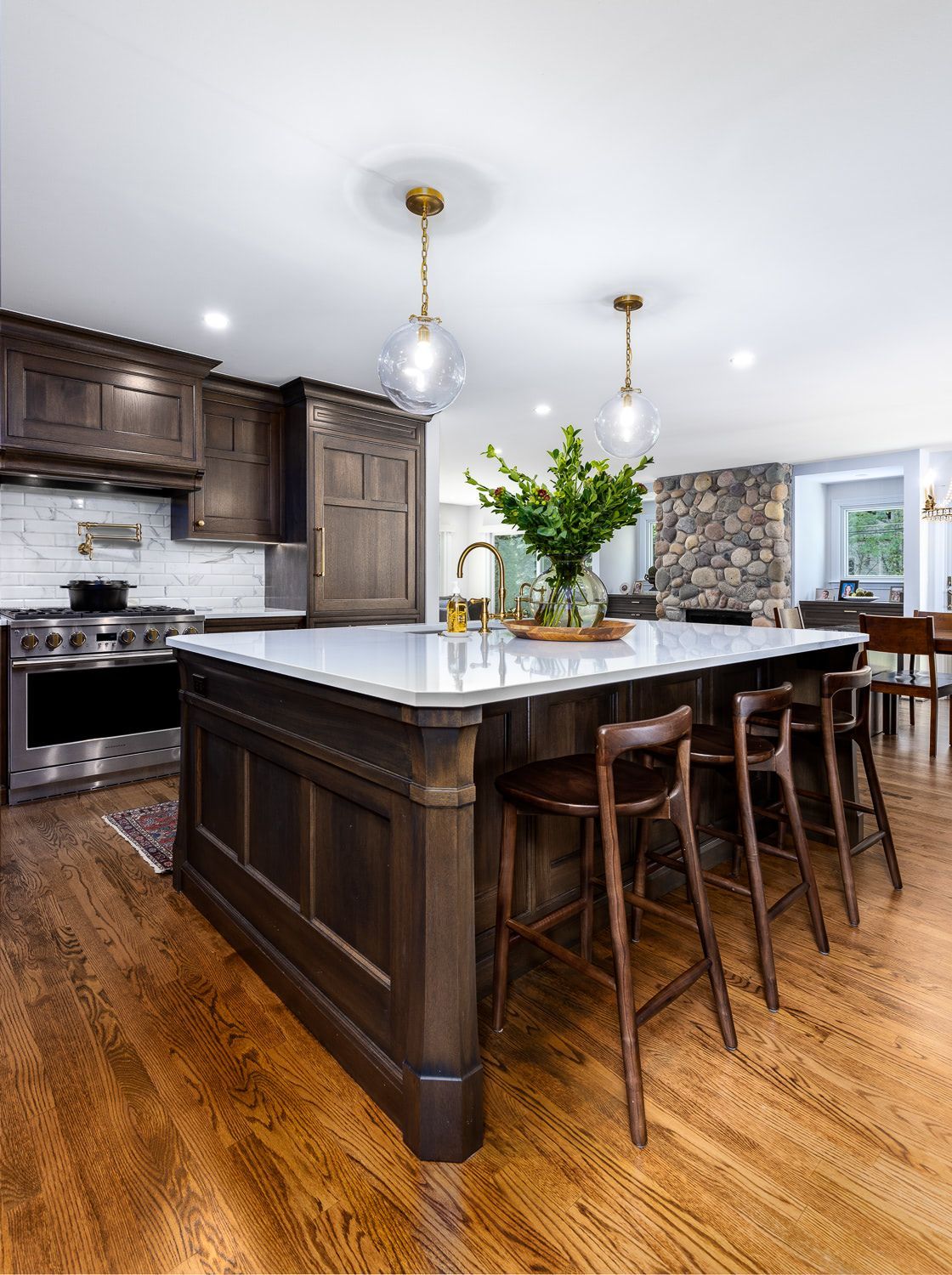 A wooden deck along the back of a house leading to a door and room with a wall of windows.
