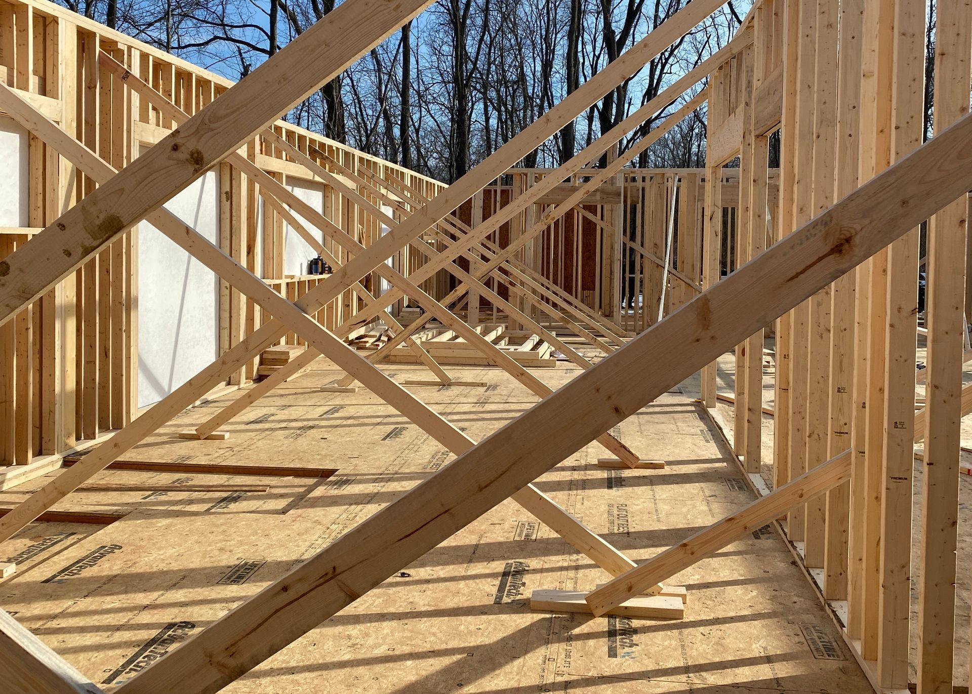 A wooden deck along the back of a house leading to a door and room with a wall of windows.