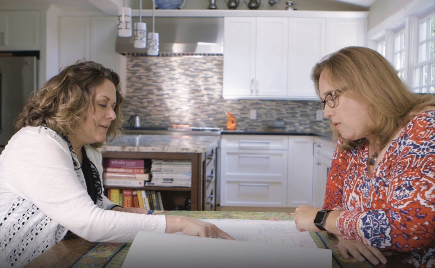 Two women are sitting at a table in a kitchen looking at a piece of paper.