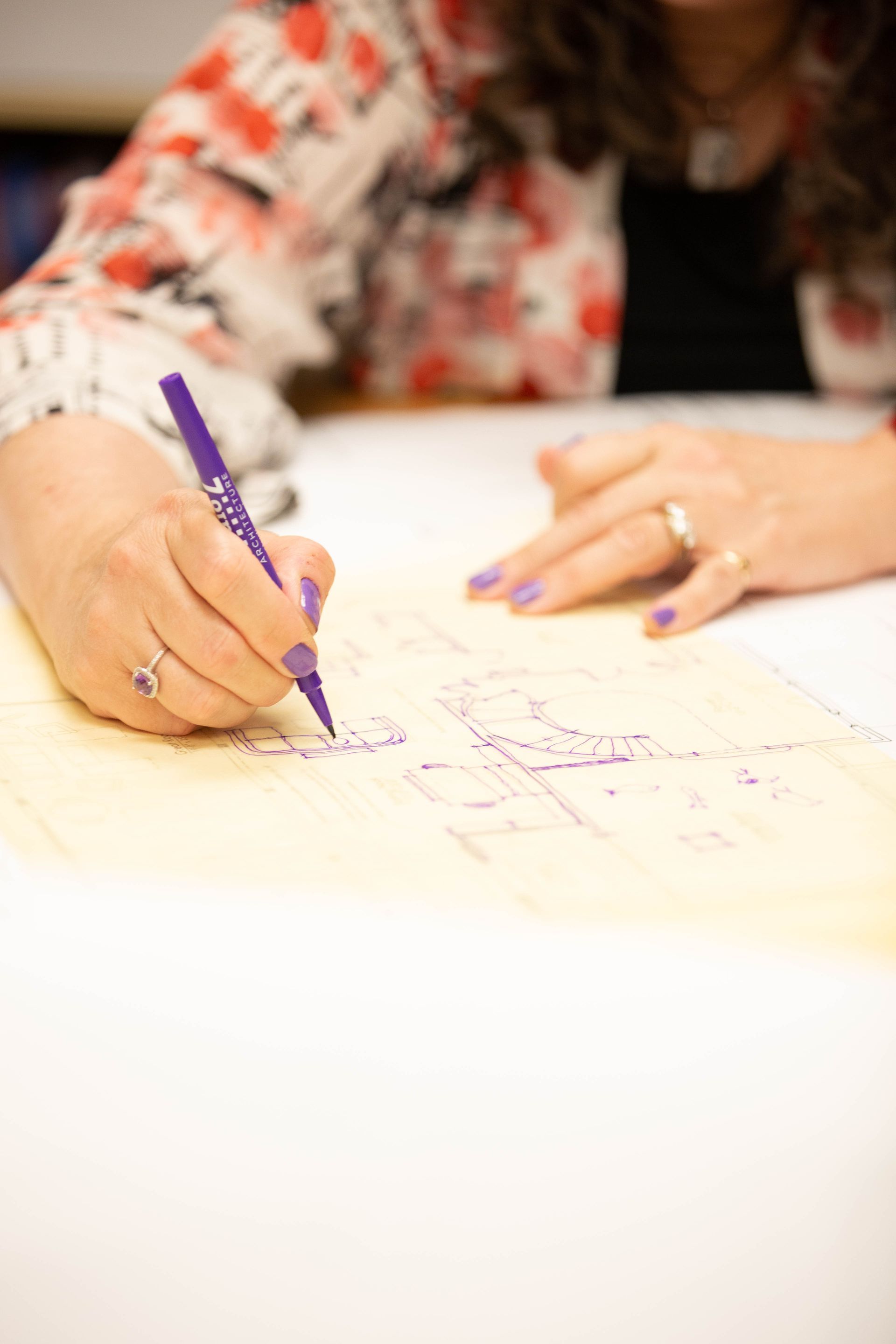 A woman is writing on a piece of paper with a purple marker.
