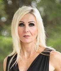 A woman with blonde hair is wearing a black dress and looking at the camera.