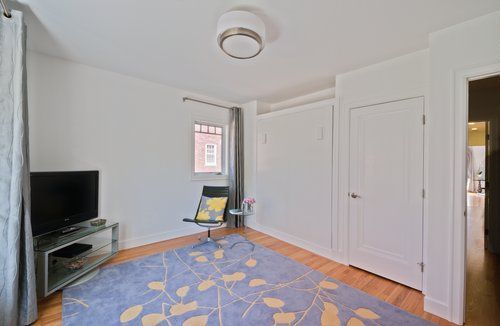 A living room with a rug , chair , television and a window.