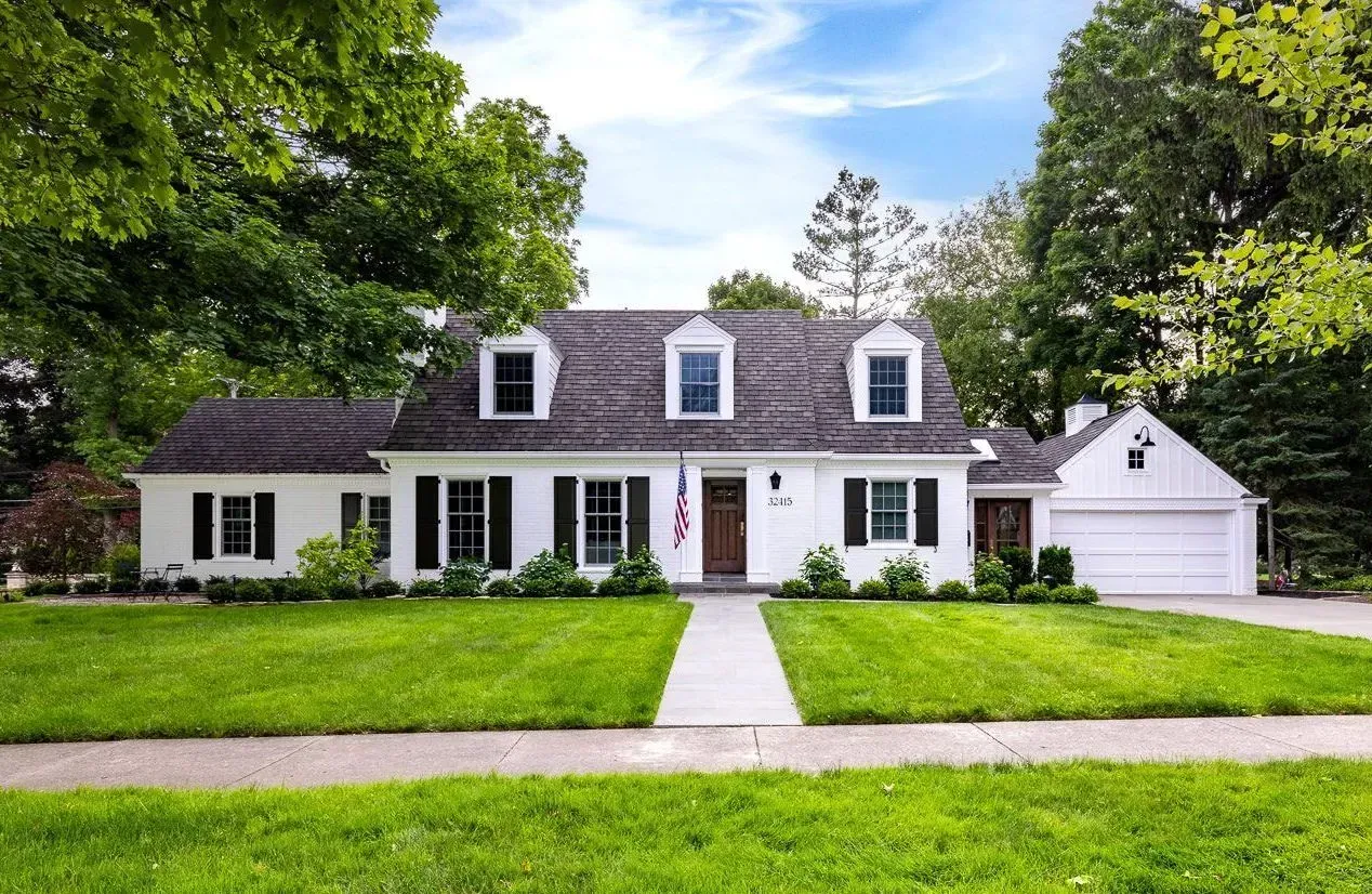 White house with dark roof, front lawn, and a detached garage under a bright blue sky