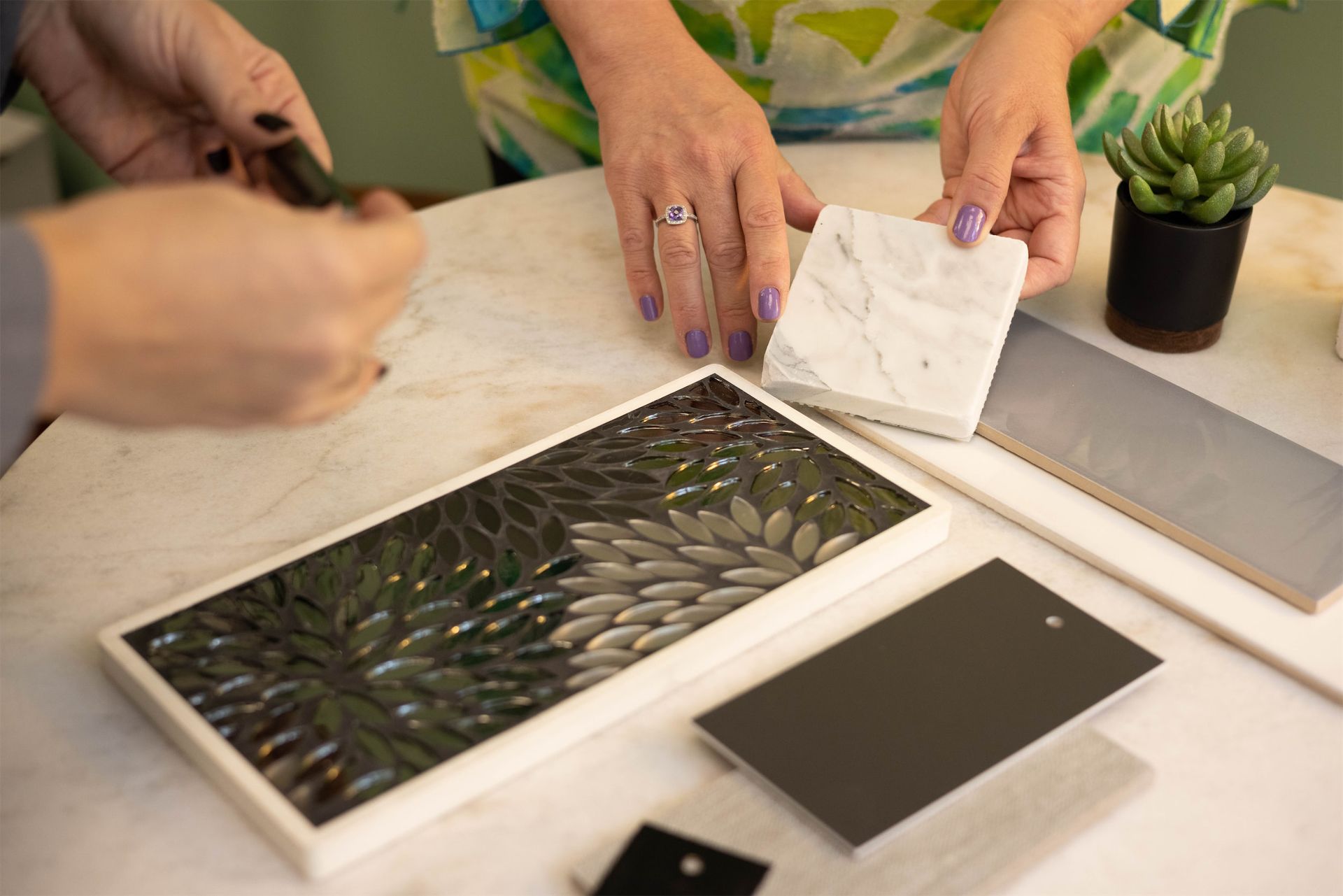 A woman is sitting at a table holding a piece of tile.