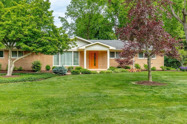 A brick house with a large lush green lawn in front of it.