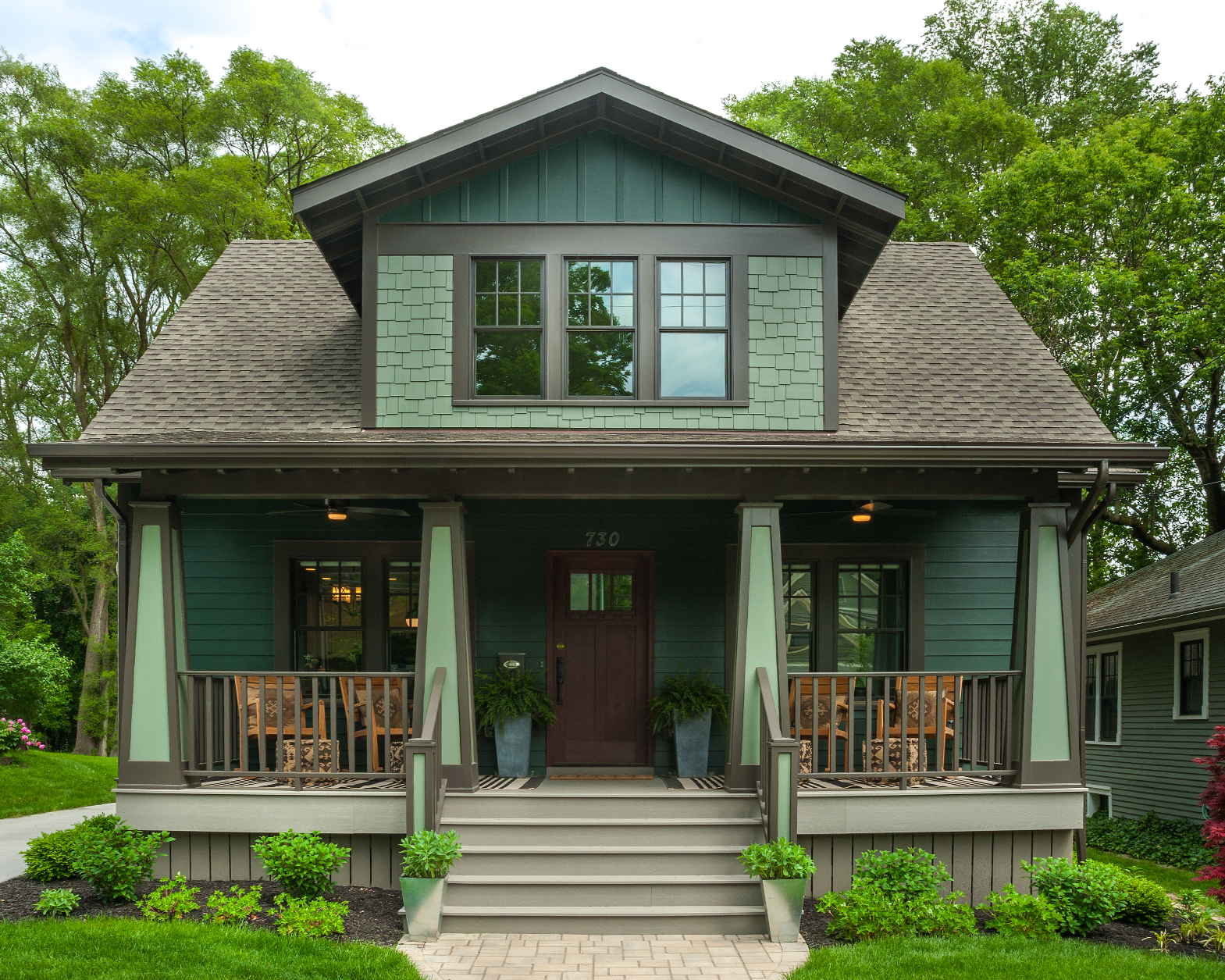 A green and brown house with a porch and stairs
