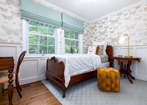 A bedroom with a bed , desk , ottoman and window.