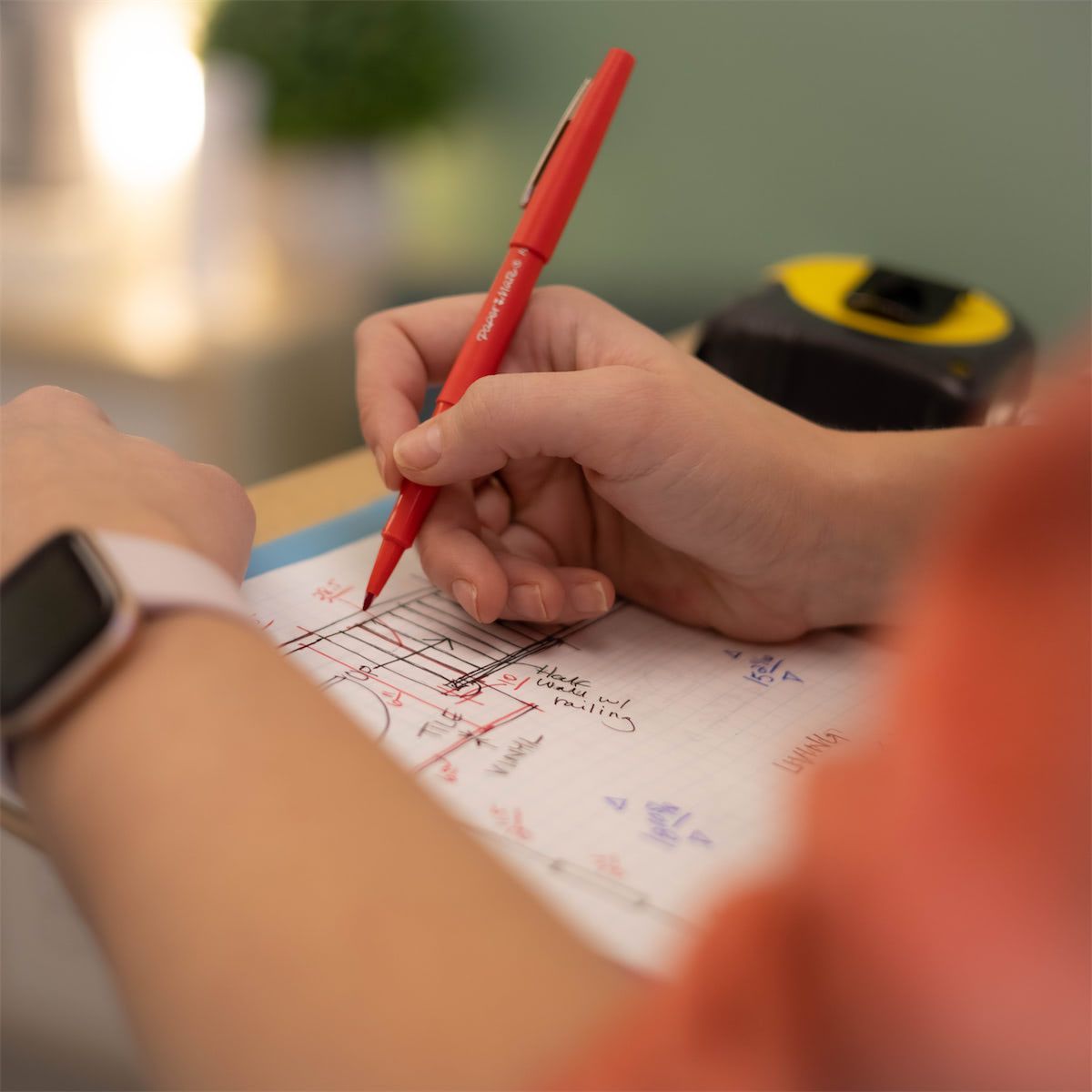 A person is writing on a piece of paper with a red pen