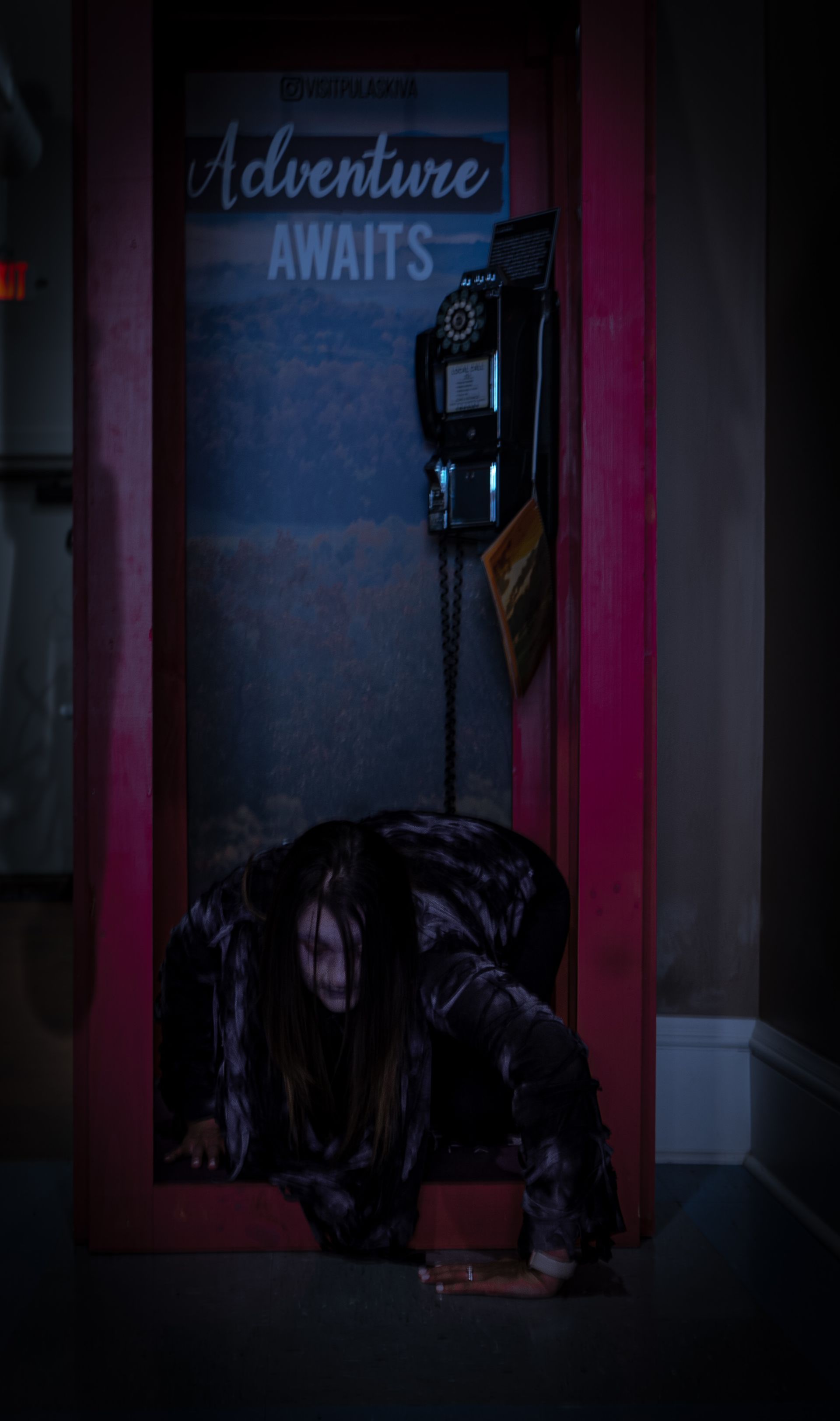 A person, covered in black, crawls out of a pink framed display with a vintage telephone and 