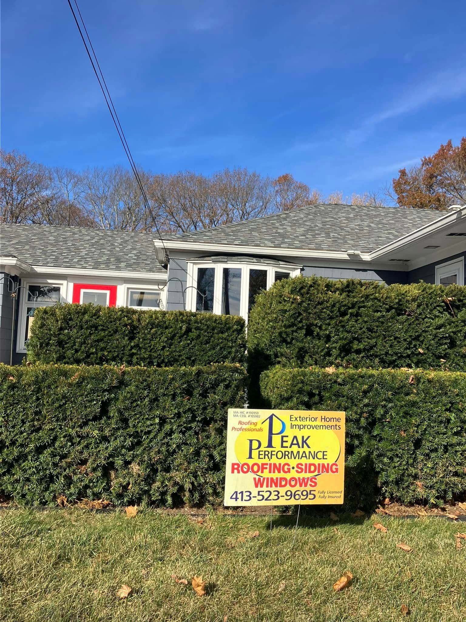 Yellow lawn sign in front of a house, reading Peak Roofing with phone numbers. Yellow lawn sign in front of a house, reading Peak Roofing with phone numbers.