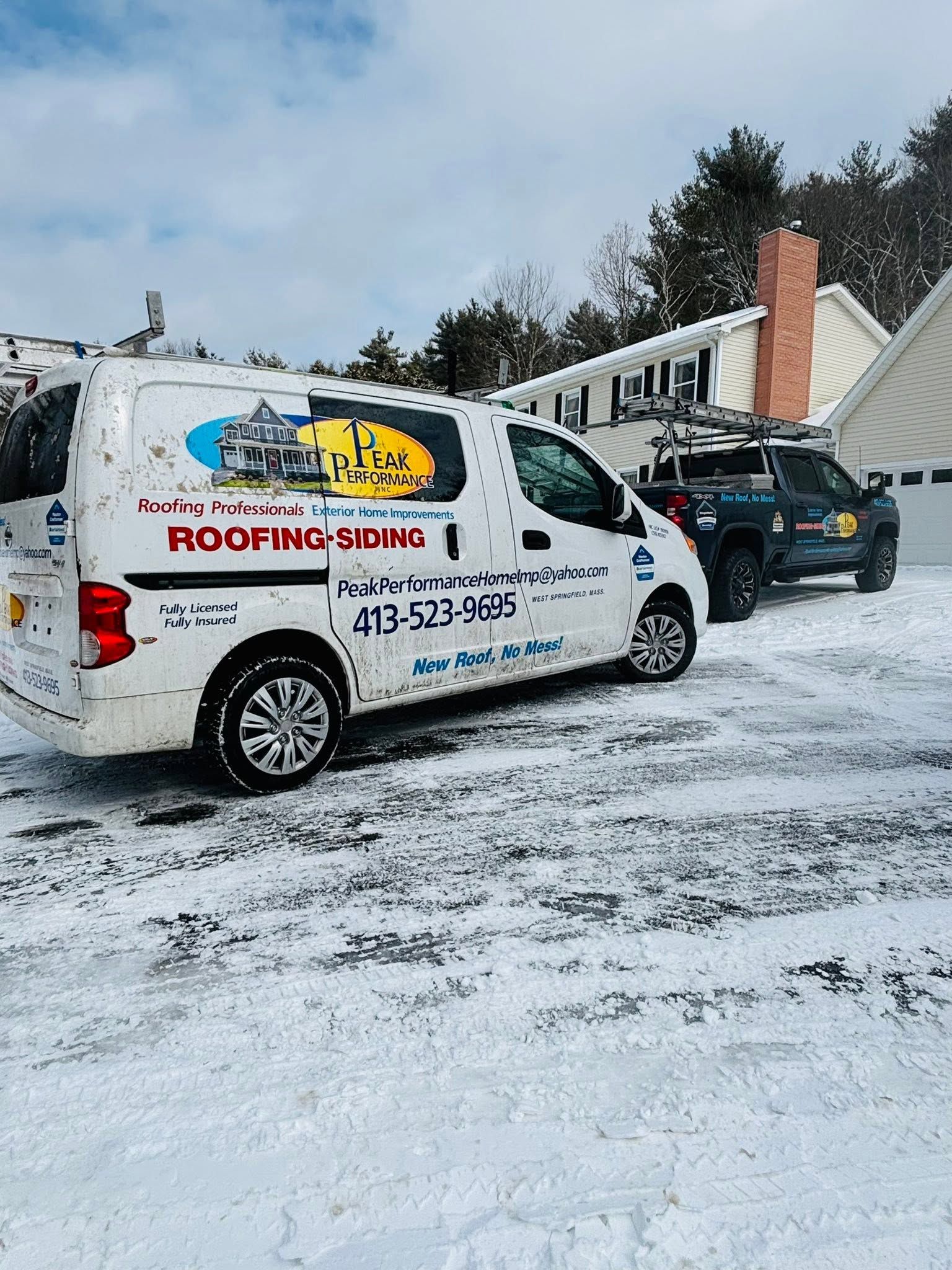 White roofing company van and black car parked in a snowy driveway by a house roof White roofing company van and black car parked in a snowy driveway by a house roof