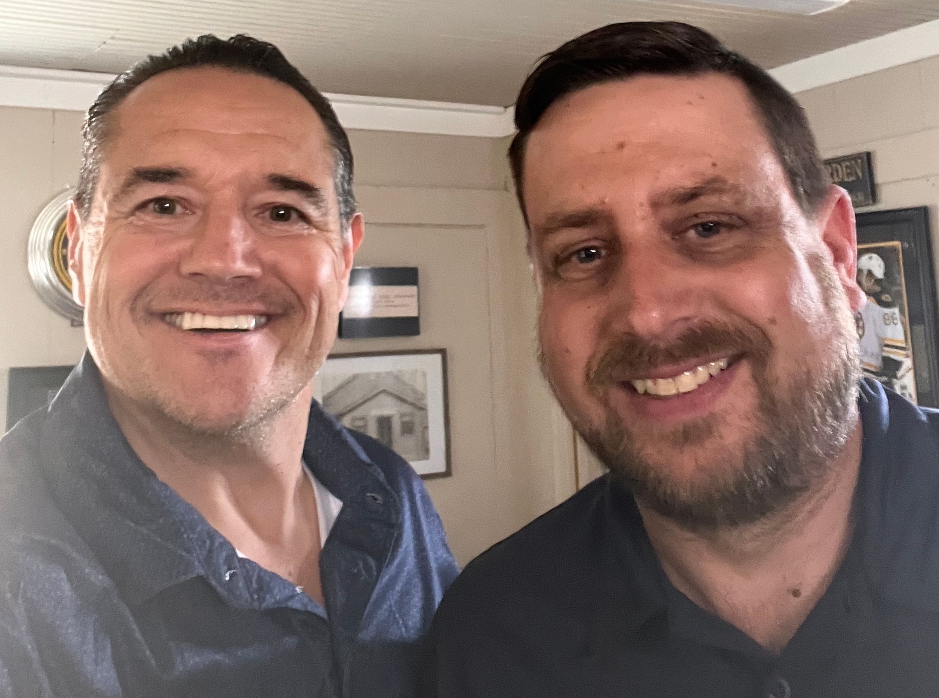 Two smiling men posing indoors, one in a blue shirt and one in a dark shirt. Two smiling men posing indoors, one in a blue shirt and one in a dark shirt.