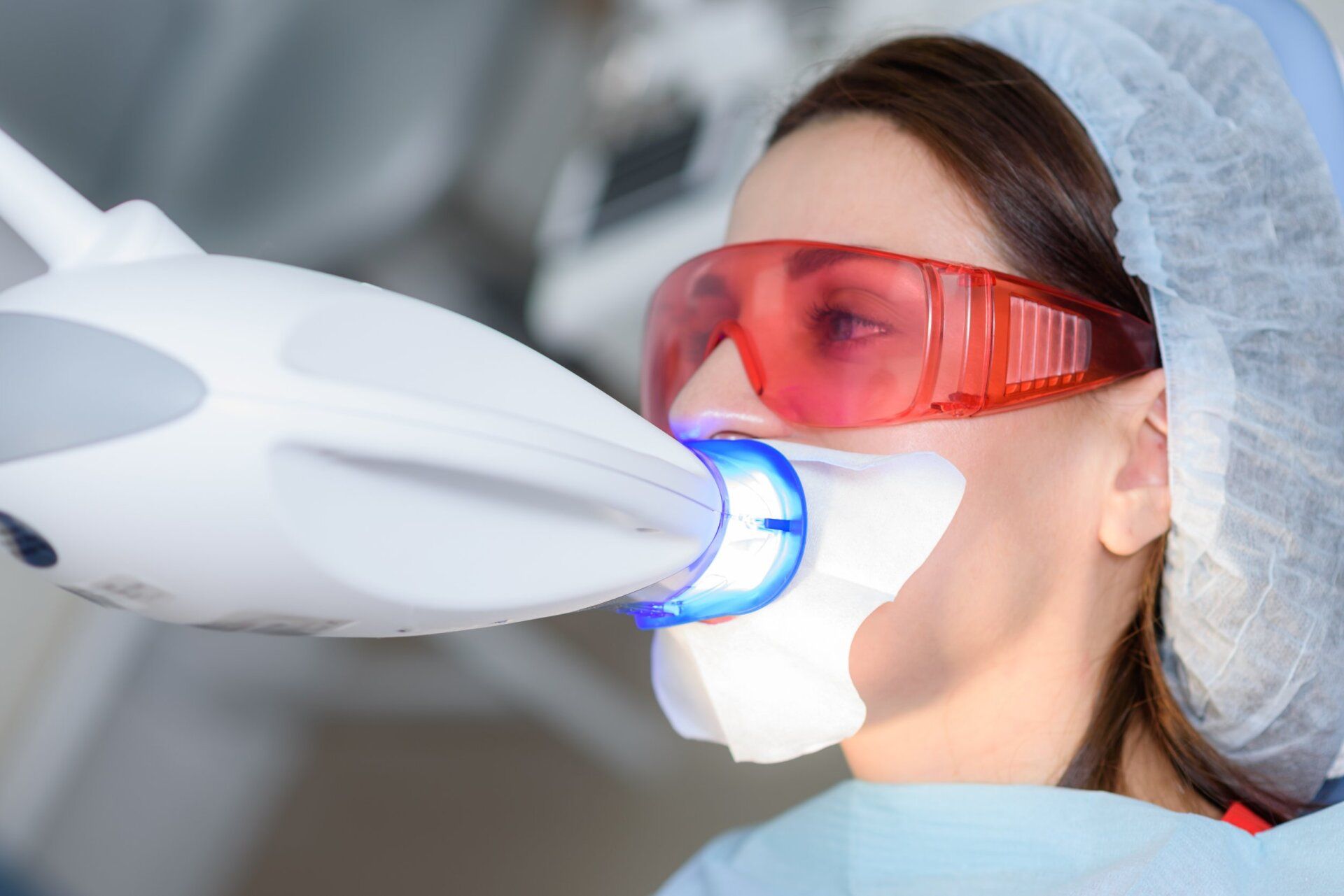The girl undergoes the procedure of teeth whitening with the help of ultraviolet lamp
