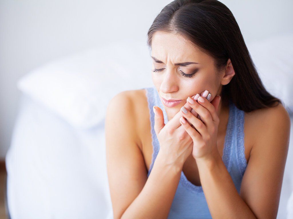 Woman grabbing her mouth while sitting on the bed because of a toothache