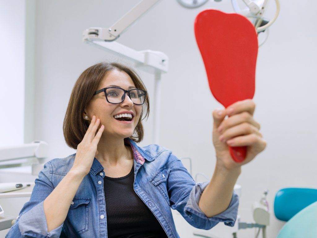 woman holding up a red mirror looking happily at her teeth