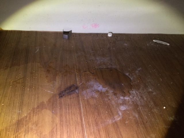 A person is holding a flashlight over a dirty wooden floor.