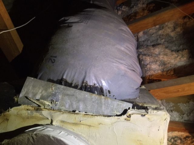 A bag of plastic is wrapped around a pipe in an attic.