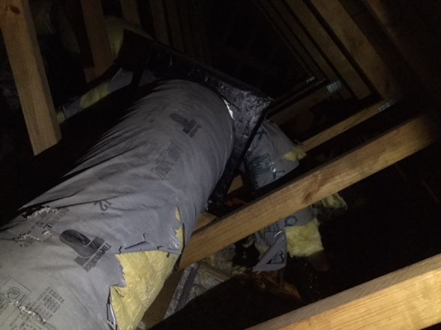 A bag of insulation is wrapped around a pipe in an attic.