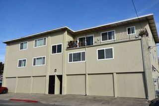 Three-story beige apartment building with garage doors and balconies on a sunny day