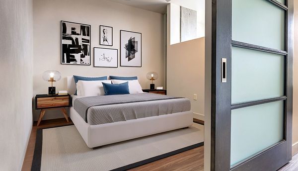 Bedroom with queen bed, artwork, bedside tables, sliding frosted glass door, beige walls, and wood floors.