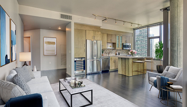 Modern apartment living room with open kitchen, stainless steel appliances, and dark wood floors.