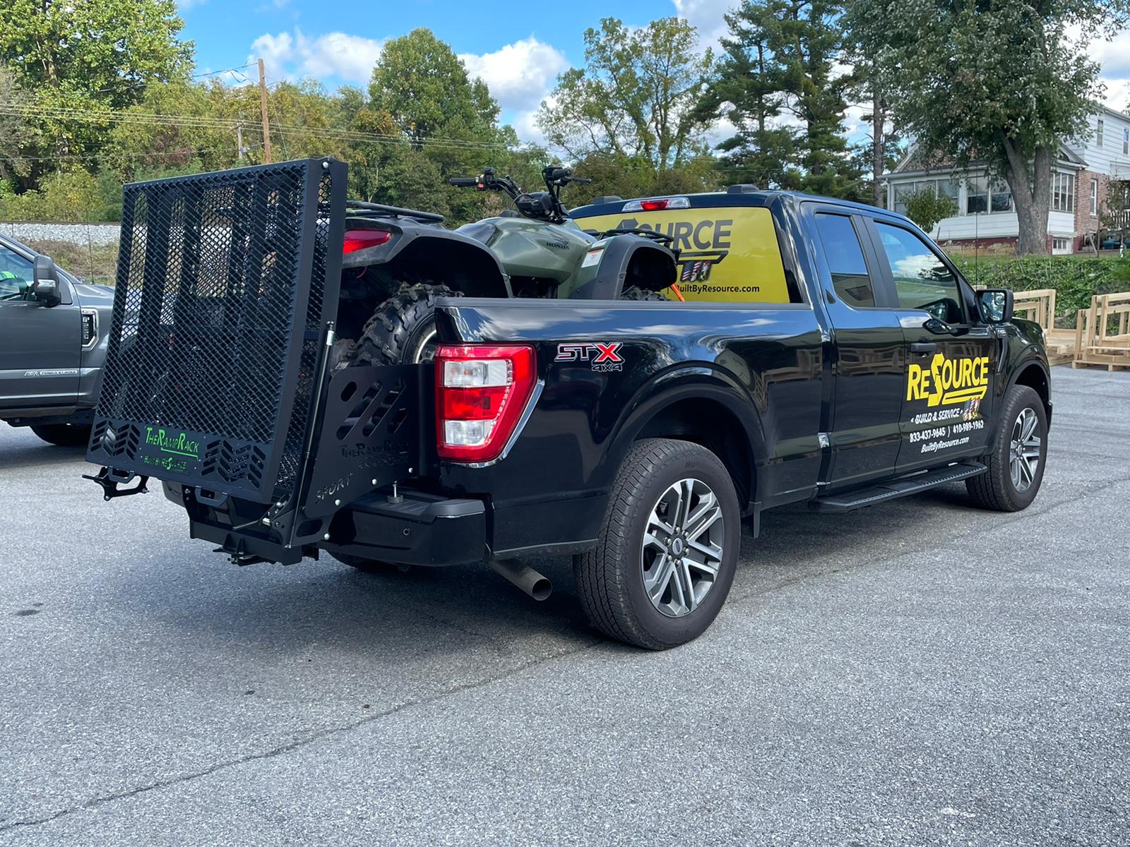 A black truck with a trailer attached to the back is parked in a parking lot.