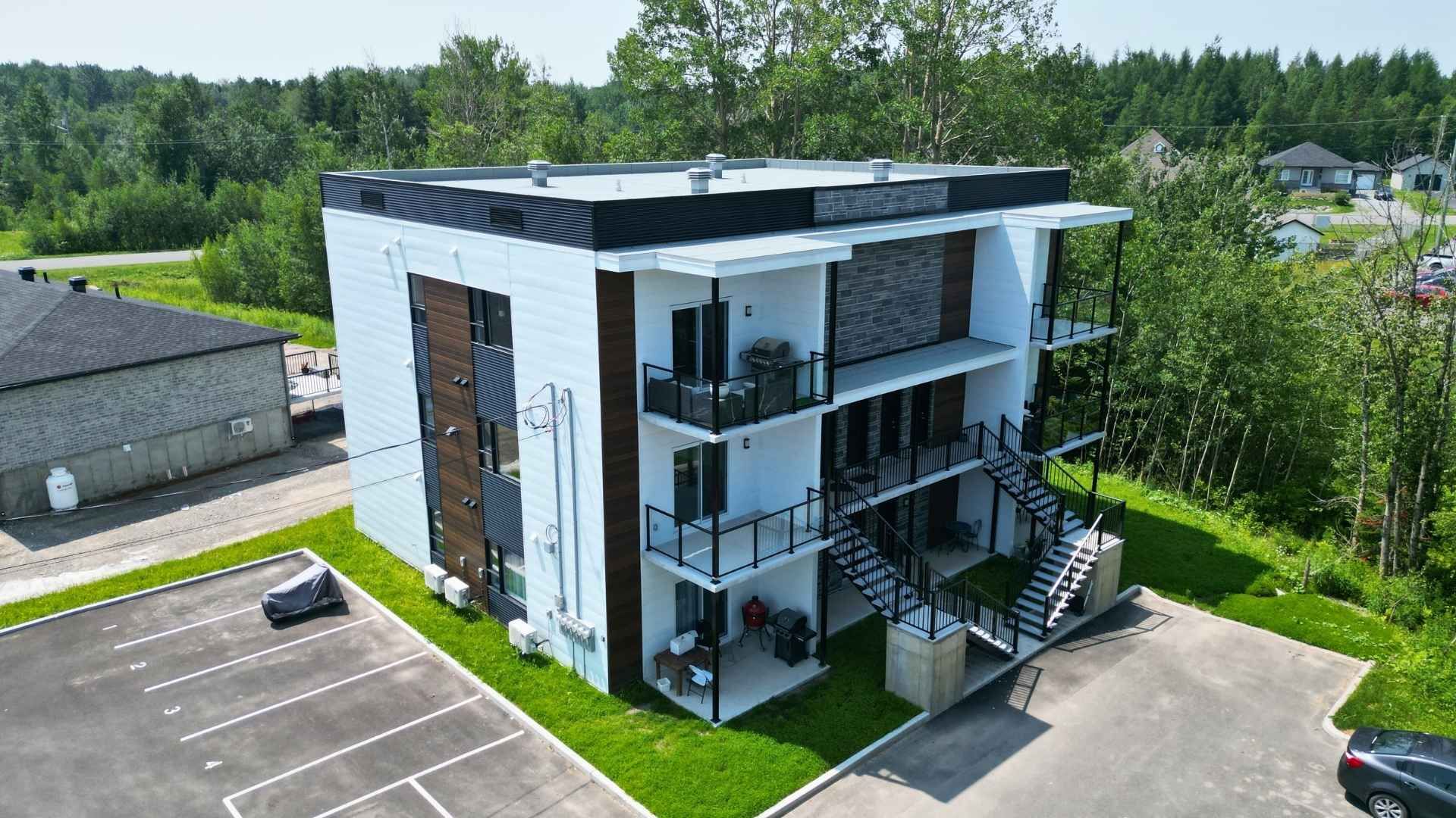 Immeuble d'appartements moderne de trois étages avec balcons, escalier extérieur et parking.