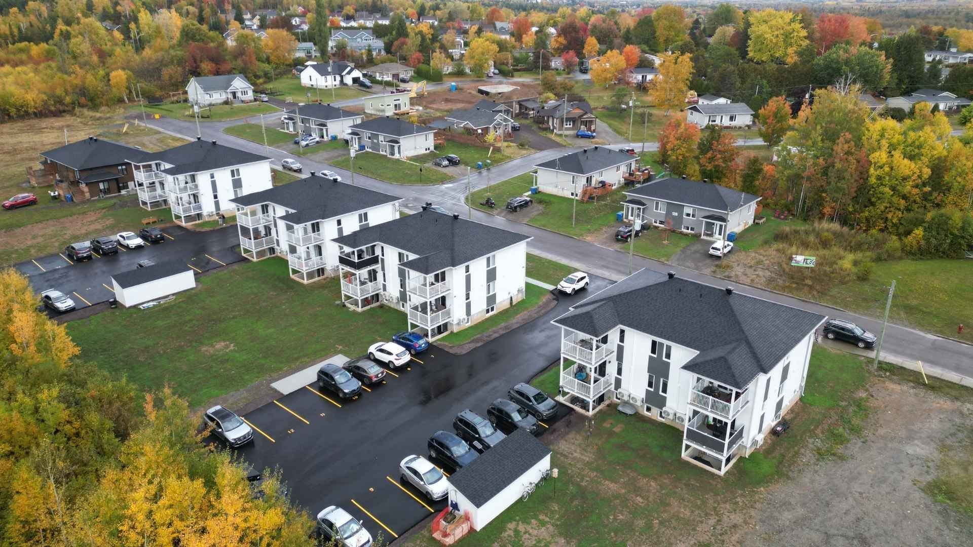 Vue aérienne d'immeubles d'appartements aux toits noirs et aux façades blanches, entourés d'arbres aux couleurs d'automne.