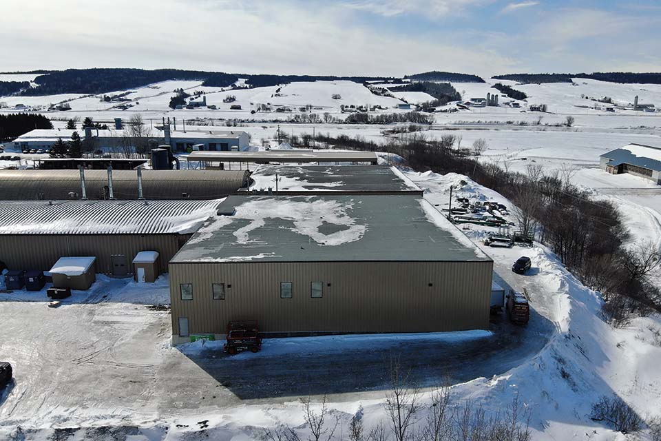 Une vue aérienne d'un grand bâtiment  industriel au milieu d'un champ enneigé.