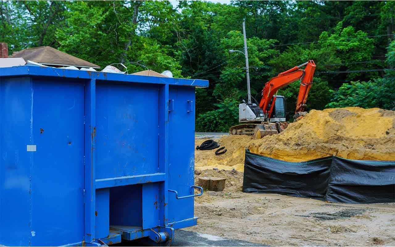une benne bleue est garée devant un chantier de construction avec un bulldozer en arrière-plan.