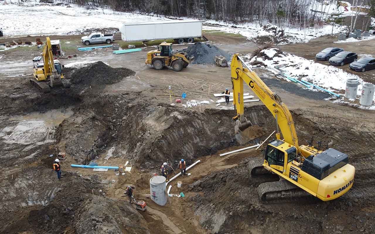 une vue aérienne d'un chantier de construction avec une excavatrice jaune creusant un trou.