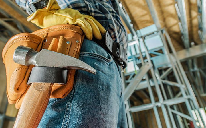 un ouvrier du bâtiment porte une ceinture à outils avec un marteau et des gants.