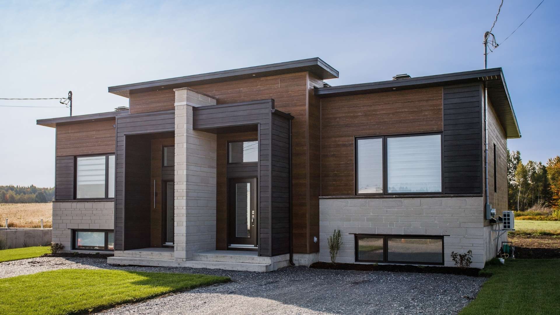 Jumelé moderne en briques et en pierres noir et marron avec un ciel bleu et une allée en gravier.